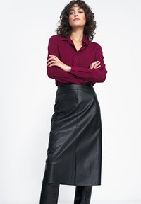 Czarna skórzana spódnica midi o gładkiej fakturze, zestawiona z bordową koszulą na guziki. Outfit wyróżnia się dopasowaną sylwetką i długimi rękawami.