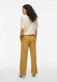 Top de encaje crema con mangas cortas combinado con pantalones de pierna ancha mostaza. Texturas y patrones notables en el top, tela suave en los pantalones.