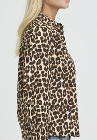 Bluză cu imprimeu leopard dintr-un material ușor, cu guler și croi lejer. Scheme de culori în nuanțe de maro închis și bej, cu modele distincte.