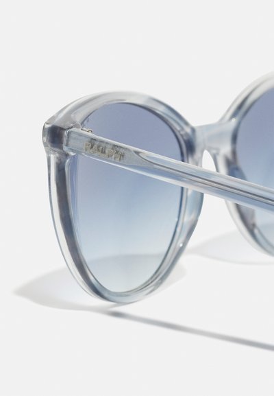 Ochelari de soare rotunzi cu un cadru transparent de culoare albastru deschis și lentile gri cu degradeu. Caracteristicile includ brațe cu marcă și o textură netedă.