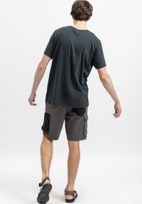 Grijze katoenen T-shirt met ronde hals, gecombineerd met cargo shorts met donkere zakken en opgerolde hemden. Footwear: bruine sandalen met banden.