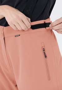 Lichtroze ritssluitingen met een gladde textuur. Beschikt over een haak-en-lus sluiting bij de taille en een zijzak met een rits.