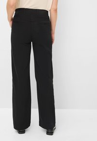 Zwarte wijde broek met hoge taille, voorzien van twee achterzakken en een gladde textuur. De zoom is lichtjes versleten.