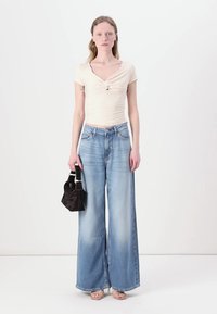 Top beige chiaro a maniche corte con dettaglio annodato, abbinato a jeans a gamba larga blu sbiaditi e una piccola borsa nera. Tacchi a strappo rosa.