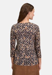 Koszulka w zwierzęcy wzór z rękawami o długości trzech czwartych, z okrągłym dekoltem. Wykonana z miękkiego materiału w odcieniach beżu, brązu i granatu.