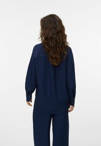 Camicia a maniche lunghe blu navy realizzata in tessuto testurizzato, con yoke posteriore e polsini con bottoni, vista da dietro.