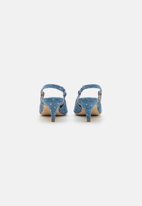 Denim slingback heels feature a textured blue upper, a small block heel, and adjustable ankle strap. Light tan inner lining and sole visible.