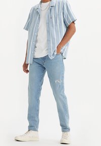 Kortärmad, ljusblå randig skjorta med bröstficka, i kombination med ljusblå slitna jeans och vita sneakers.