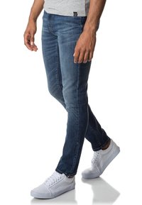 Džínové kalhoty v tmavě modré barvě, slim-fit střihu s jemným vyblednutím. V kombinaci s bílými teniskami, které mají nízký profil a šněrovací uzavření.