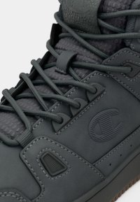 Szare buty z teksturowaną skórzaną cholewką, wyraźnym logo i okrągłymi sznurowadłami. Posiadają wyściełany język oraz gumową podeszwę z małymi perforacjami.