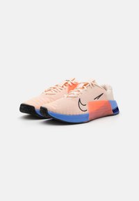 Zapatillas de malla ligeras en melocotón, con un logo negro, entresuela naranja y un acento azul en la suela. Diseño texturizado para una mayor transpirabilidad.