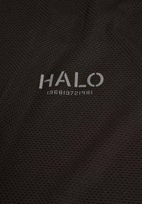 Un tissu texturé noir présente un motif en maille. Le logo "HALO" et les chiffres "196819721981" sont imprimés en gris clair.