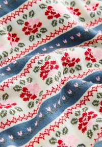 Gestrickter Stoff mit Reihen von roten und rosa Blumenmustern und grünen Blättern, getrennt durch blaue Bänder mit kleinen rosa Blütenmotiven.