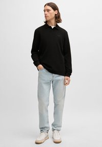 Polo preto de manga longa com colarinho, combinado com jeans azul claro e sapatilhas brancas. O polo apresenta uma marcação subtil no peito.
