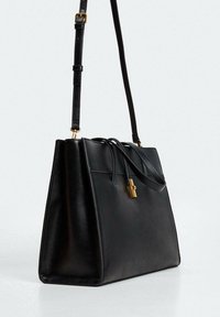 Černá kožená kabelka se strukturovaným designem, horními rukojeťmi a odnímatelným popruhem. Obsahuje klips na zlatém kovovém hardware a ozdobné šňůrky.