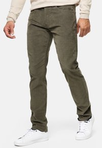 Olivengrønne cordbuks, der har en slim fit, fem lommer og en struktureret overflade. Sammen med hvide sneakers.