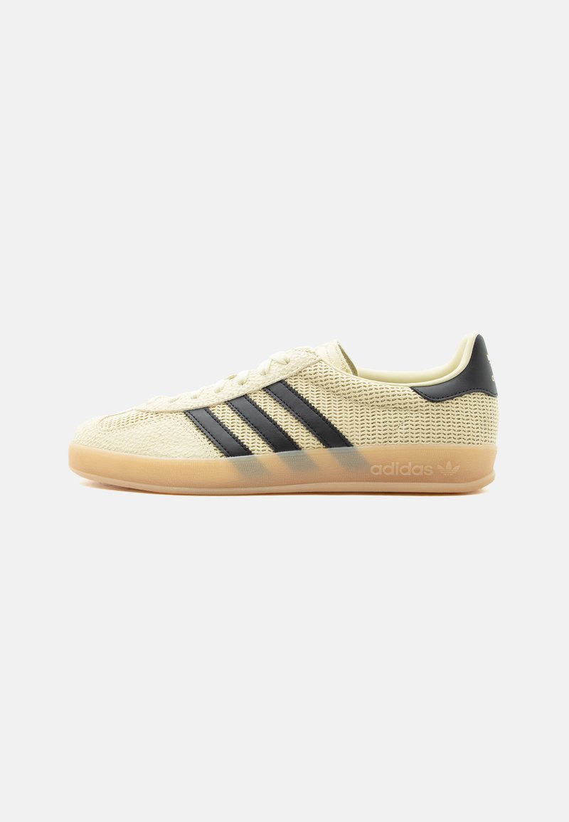 Αθλητικό παπούτσι Adidas σε κρεμ διαφάνεια με μαύρες τρεις ρίγες και λαστιχένια σόλα, πλευρική όψη σε απλό ανοιχτό φόντο.