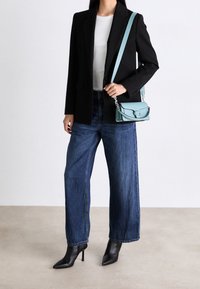 Schwarzes Blazer, weißes Hemd, weite blaue Jeans und schwarze High-Heels-Stiefel. Eine kleine hellblaue Umhängetasche mit Kettenakzenten.