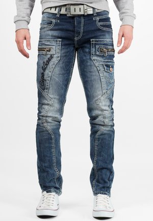 Jean en denim bleu avec une finition délavée, poches zippées et surpiqûres contrastantes. Comprend un texte brodé et une coupe droite.
