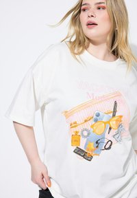 Hvid oversized t-shirt med et trykt design af ferieting i orange og blå nuancer, herunder solbriller, parfumeflaske og en telefon.