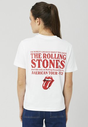 T-shirt en coton blanc arborant un texte rouge indiquant "THE ROLLING STONES" et un logo avec un dessin de langue et de lèvres. Coupe décontractée.