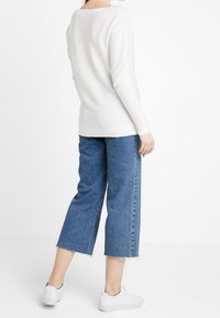 Vit stickad tröja med långa ärmar, tillsammans med högmidjade blå denimjeans med raw hem. Vita sneakers fulländar looken.