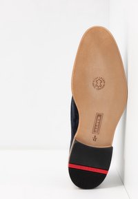 Semelle de chaussure en daim noir avec une lanière intérieure en cuir de couleur claire. Étiquettes en relief et une ligne d'accent rouge près du talon. Taille 42.