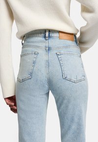 Jeans in denim blu chiaro con vita alta, dotati di due tasche posteriori e di un'etichetta in pelle sul girovita. La texture appare leggermente sbiadita.