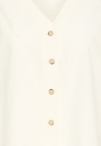 Vêtement en tissu blanc avec encolure en V et quatre boutons ronds beige alignés verticalement au centre.