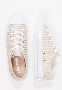 Bežovo-bílé kárované tenisky Converse s bílými tkaničkami, gumovými špičkami a bočními ventilačními otvory zobrazené z horního a bočního pohledu.