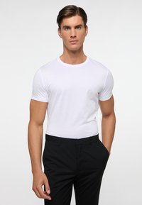 Witte, aansluitende t-shirt met korte mouwen, ronde hals, gecombineerd met zwarte broek. Glad uithouding, minimalistisch ontwerp, geen zichtbare patronen of logo's.