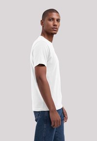 Weißes Baumwoll-T-Shirt mit Rundhalsausschnitt und kurzen Ärmeln, mit lockerer Passform. Getragen mit blauen Jeans im Seitenblick.