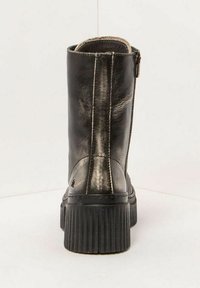 Bottine en cuir noir avec semelle épaisse à rainures et fermeture éclair latérale visible, montrée de l'arrière sur un fond clair.