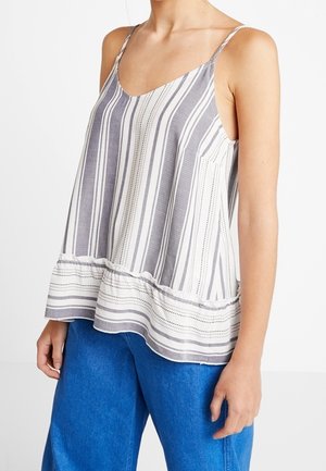 Tílko bez rukávů s volným střihem, šedobílými vertikálními pruhy, párované s jasně modrými širokými kalhotami na stojící osobě.