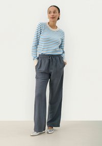 Blauw en beige gestreepte sweater met lange mouwen gecombineerd met donkergrijze wijde broek. De outfit heeft een elastische tailleband en zijzakken.