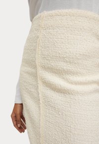 Knee-length krämfärgad kjol gjord av strukturerad tyg med en något fransad fåll och synliga sid sömdetaljer.