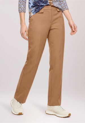 Personne portant un pantalon marron droit, des baskets blanches et un haut à motifs avec des tons bleus et marron.