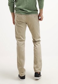 Vaaleat rentoihin housut suoran leikkauksen kera, joissa on takataskut, yhdistettynä mustiin matalavartisiin tennareihin ja vihreään pitkänhihaiseen paitaan.