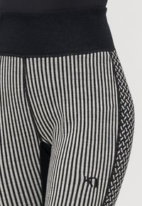 Randiga svarta och grå tights med en bred svart midja, sidopaneler med houndstooth-mönster och en synlig varumärkeslogotyp.