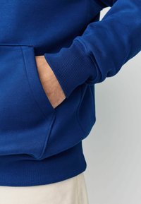 Blaues Sweatshirt mit Kängurutasche, gerippten Bündchen und Saum. Hergestellt aus einem weichen Stoff mit glatter Textur.