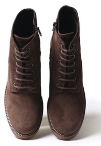 Bottines en suède marron avec un design à lacets, des zips sur le côté et un détail de couture contrasté le long de la semelle.