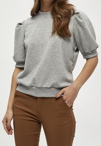 Grå tröja med rund hals, puffade korta ärmar och ribbat avslut. Matchas med bruna tajta byxor. Slät textur.