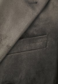 Sivi sueden materijal s glatkom teksturom, s preklopnom džepom sprijeda za praktičnost i dizajnerski detalj.
