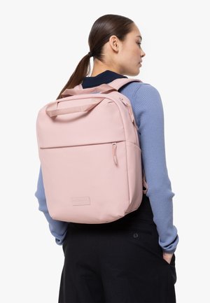 Pink backpack made of smooth material, featuring a front pocket, top handle, and adjustable straps, showcased against a neutral background.