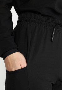 Svarta joggerbyxor med elastisk midja och snöre, sidficka och slät vävd tygstruktur.