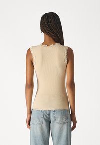 Beige vahetükiga tank top, millel on pitsaktsendid käeaukude ja dekoltee ääres, keha järgiv lõige, koos helesiniste mugavate teksadega.