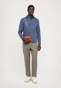 Blauwe lange mouwen shirt, knoopjes, gecombineerd met lichtgrijze geruite broek en crème sneakers. Bruine schoudertas met verstelbare riem.