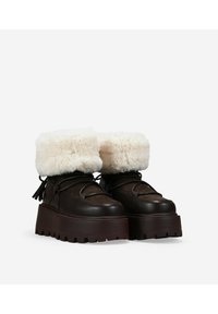 Botas de invierno marrones con un puño de crema esponjoso, que cuentan con una suela gruesa, punta redonda y cordones decorativos. Fabricadas en materiales de cuero y ante.