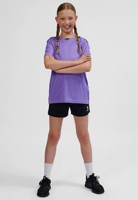 Lila sport-t-shirt med V-ringning, svarta shorts, vita strumpor och svarta sneakers. Tyget verkar slätt och lätt.