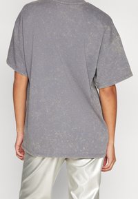 Přes velikostí šedé tričko s texturovaným, mramorovým vzorem. Krátké rukávy a žebrovaný kulatý výstřih. Kombinováno s lesklými metalickými stříbrnými kalhotami.